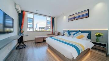 A modern hotel room with a large bed, a desk, a chair, a TV, and a window with a city view.