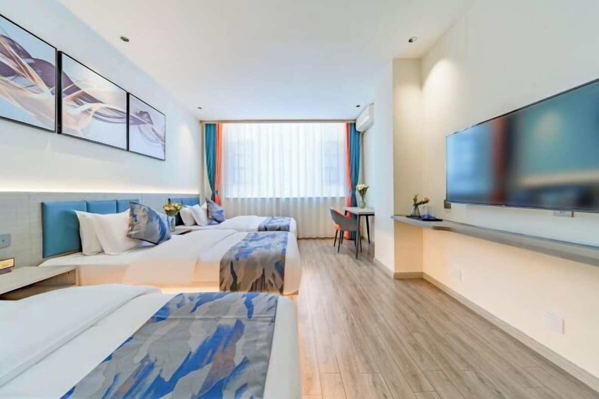 A hotel room with two beds, a TV, a desk, and a window with curtains.
