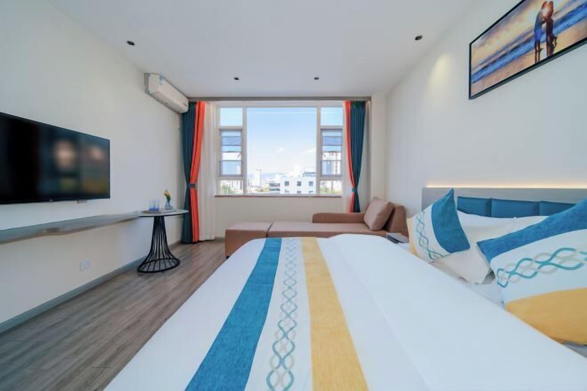A hotel room with a bed, a TV, a window with curtains, and a painting on the wall.