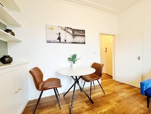 A dining area with a round table and four chairs, a potted plant, and a wall-mounted artwork.