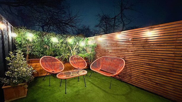 An outdoor patio area with artificial grass, wooden slatted walls, and red wicker chairs. - Stylish Kennington flat w/garden, KING bed nr tube (Greater London)