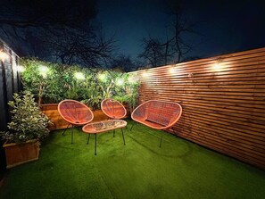 An outdoor patio area with artificial grass, wooden slatted walls, and red wicker chairs.