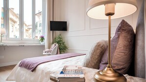 A neatly made bed with a book and a lamp, a TV on the wall, and a window with a view of buildings. - Cozy apartment with terrace suitable for families up to 6 people  (Roma)