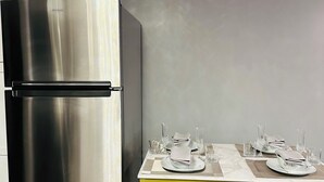 Ein Edelstahl-Kühlschrank und ein Esstisch mit Tellern, Gläsern und Besteck.