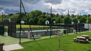 A sports court with basketball hoops, a fence, and picnic tables. - Au Sein de la Suisse Normande, Randonnée, Vélo et le Kayak Pour Tous (Pont-d'Ouilly)