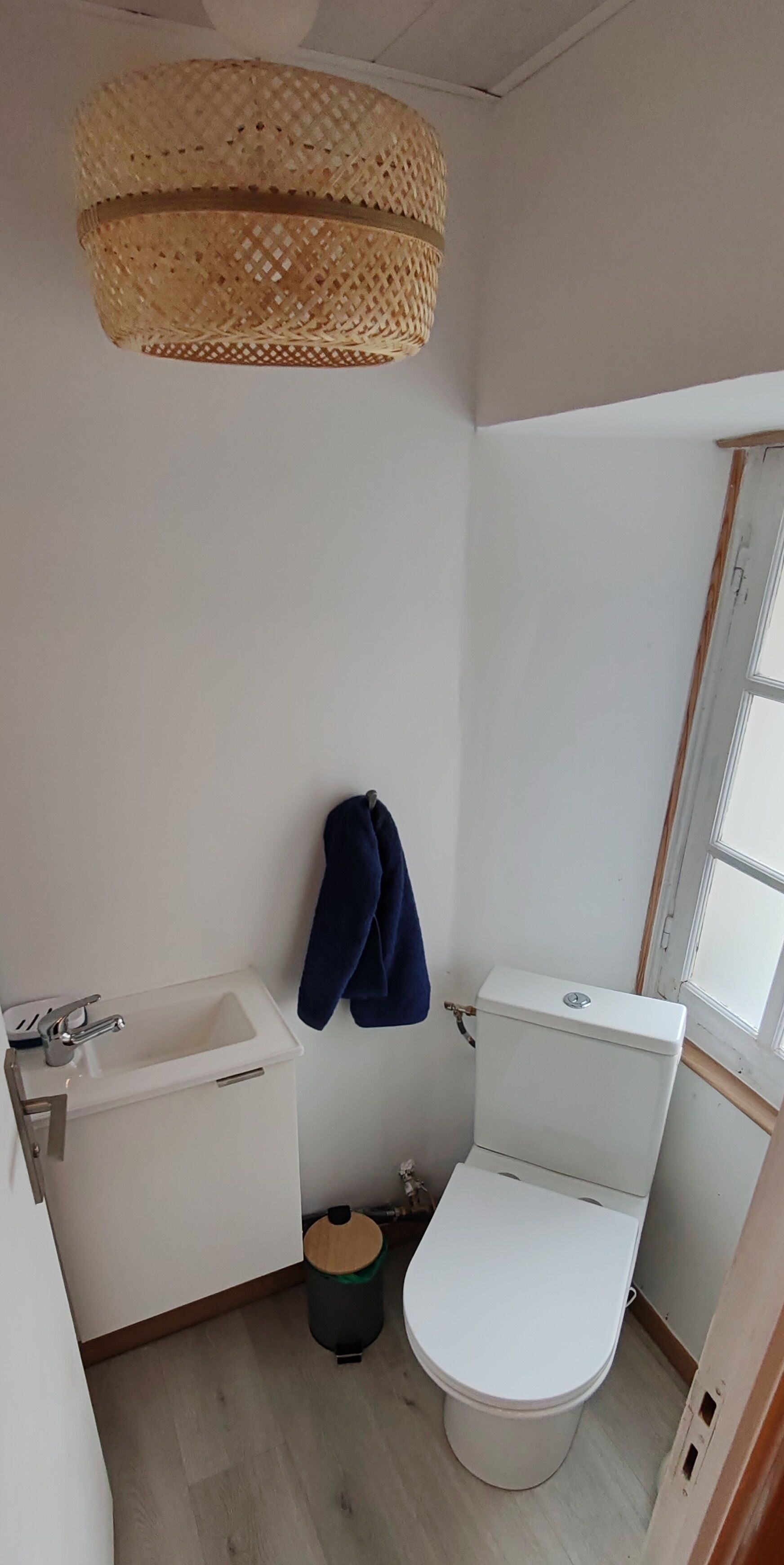 A small, compact bathroom with a white sink, toilet, and a woven ceiling light fixture.