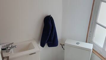 A small, compact bathroom with a white sink, toilet, and a woven ceiling light fixture.