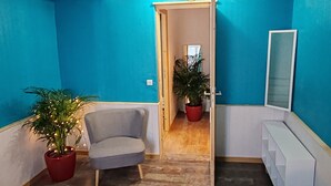 A hallway with blue walls, a grey armchair, and two potted plants. - Au Sein de la Suisse Normande, Randonnée, Vélo et le Kayak Pour Tous (Pont-d'Ouilly)