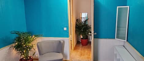 A hallway with blue walls, a grey armchair, and two potted plants.