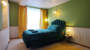 A bedroom with a bed, yellow curtains, a bedside lamp, and a wall-mounted light fixture. - Au Sein de la Suisse Normande, Randonnée, Vélo et le Kayak Pour Tous (Pont-d'Ouilly)