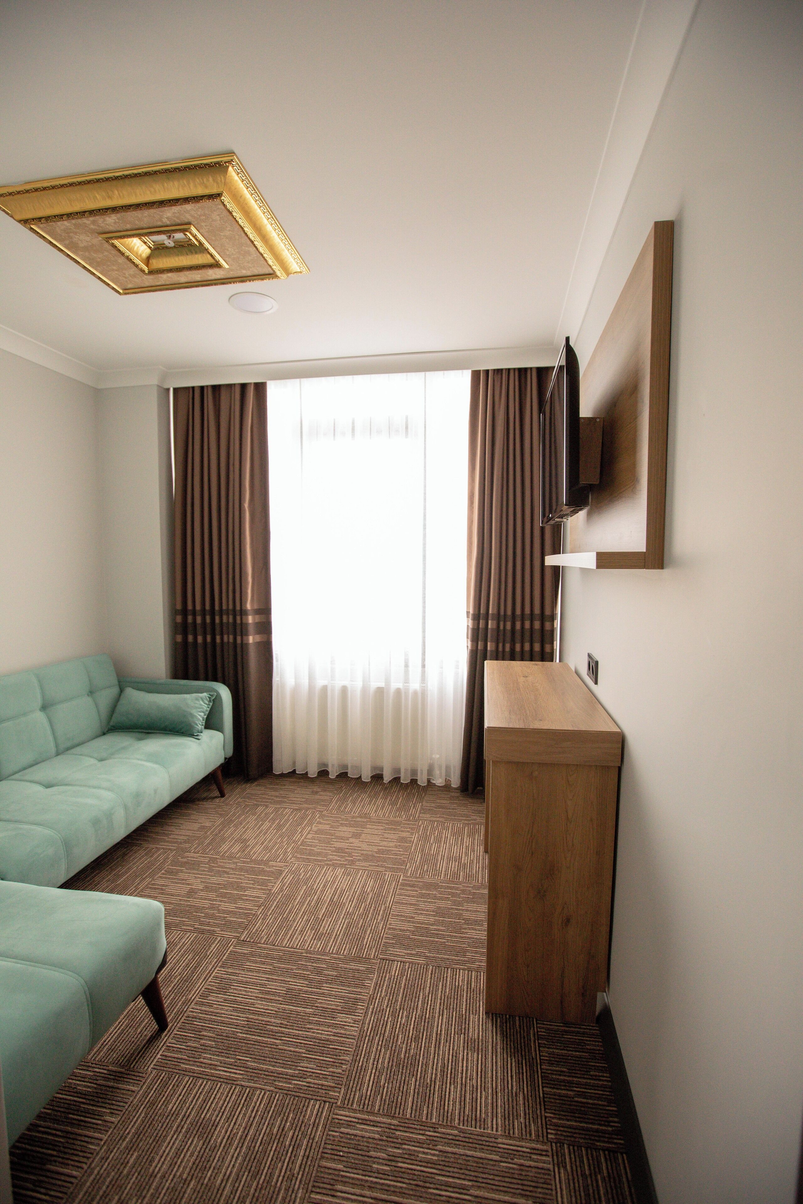 A hotel room with a sofa, a wooden side table, a flat-screen TV mounted on the wall, and a patterned carpet.