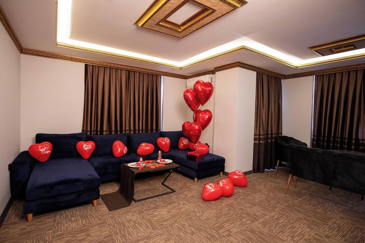A modern living room with a dark blue sectional sofa, a small coffee table, and heart-shaped balloons.