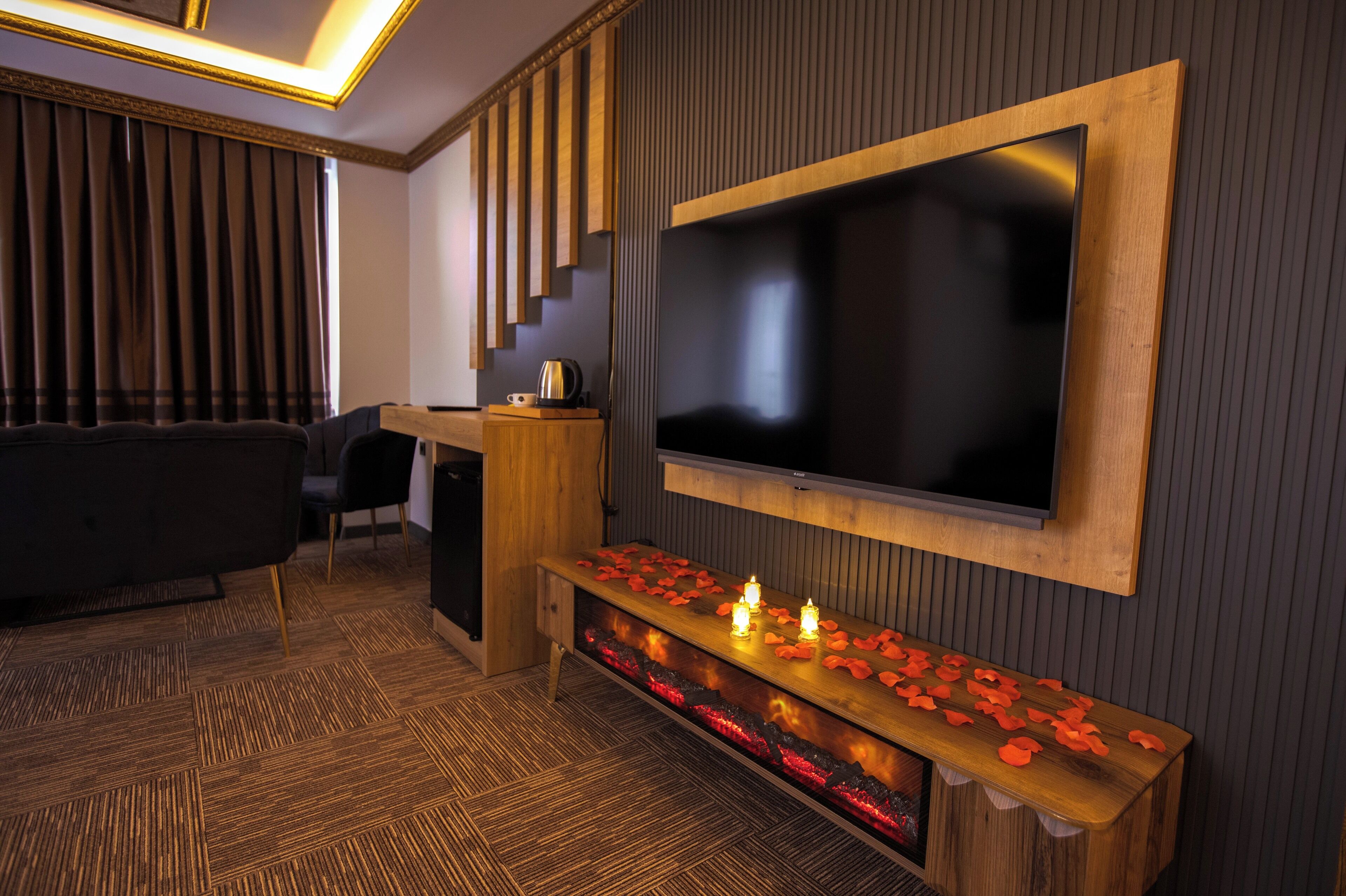 A modern living room with a large flat-screen TV mounted on a wooden wall, a dark sofa, a wooden coffee table with candles, and a patterned carpet.