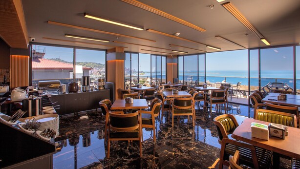Un restaurante moderno con vistas al mar, que cuenta con techos altos, amplias ventanas y un suelo de mármol pulido.