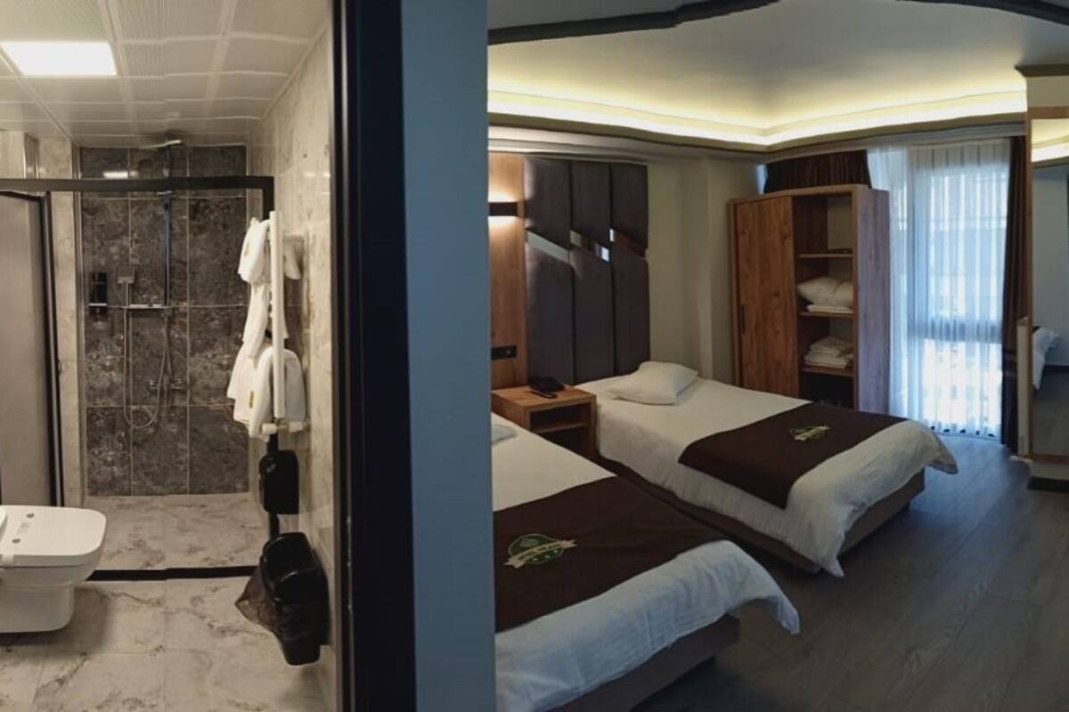 A hotel room with two single beds, a sofa, a shower area, and a TV.