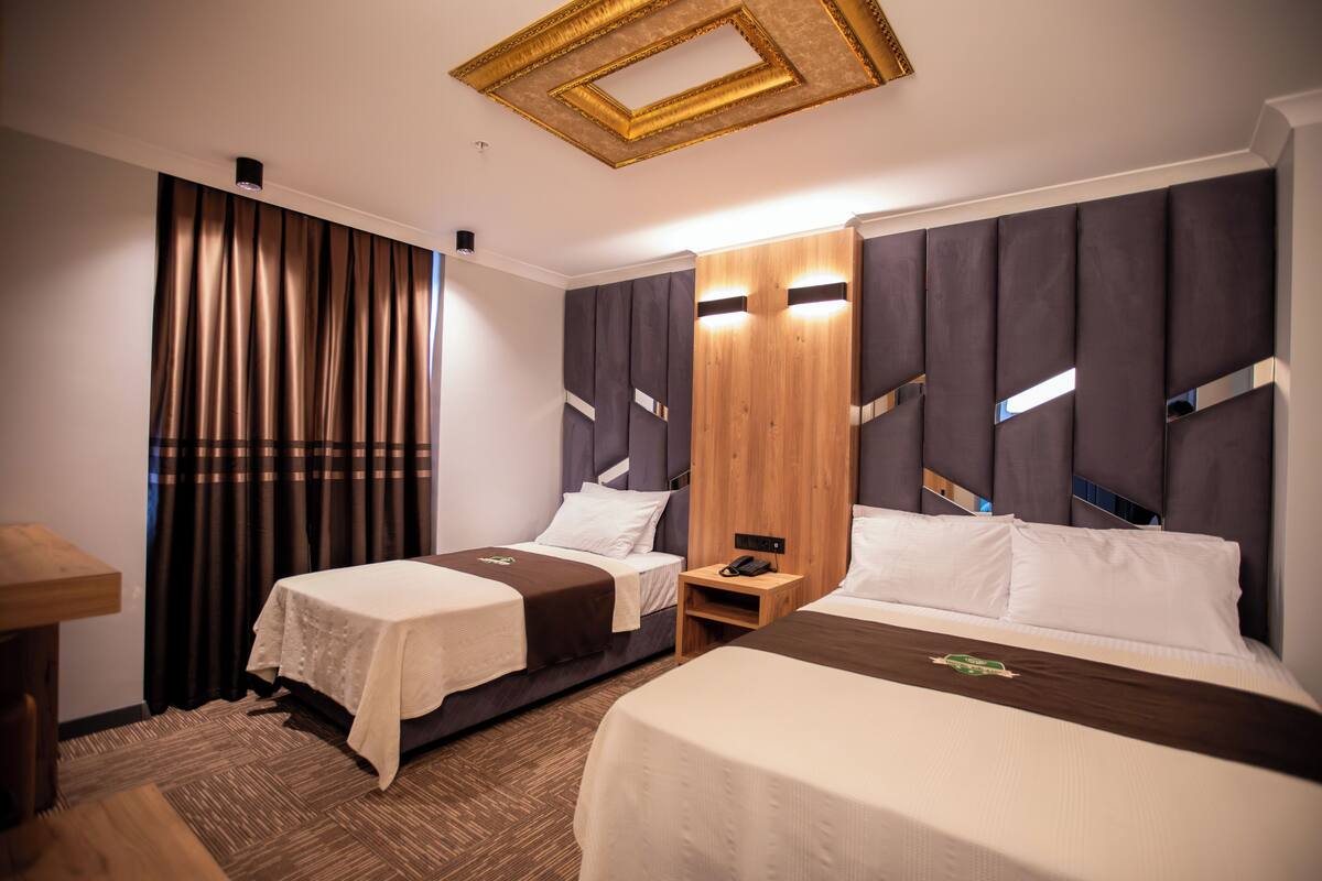 A hotel room with two beds, a wooden headboard, a nightstand, and a curtain.