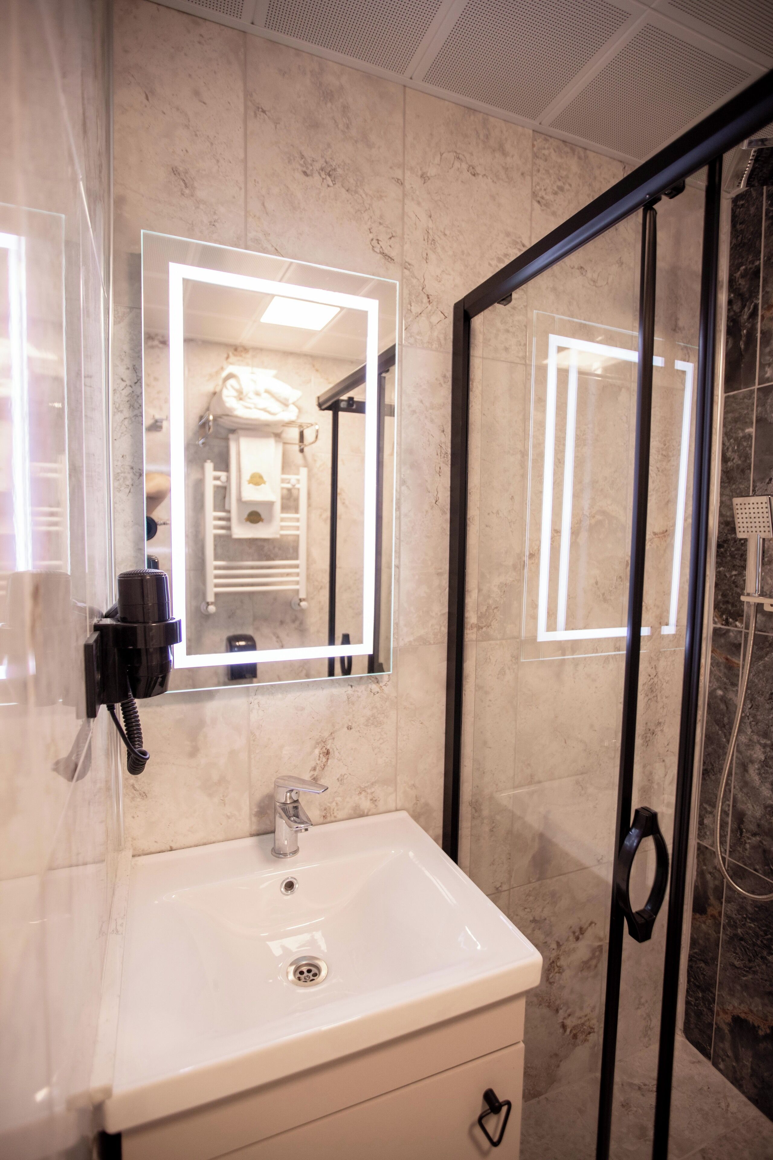 A bathroom with a white sink, a mirror with illuminated edges, and a glass shower door.
