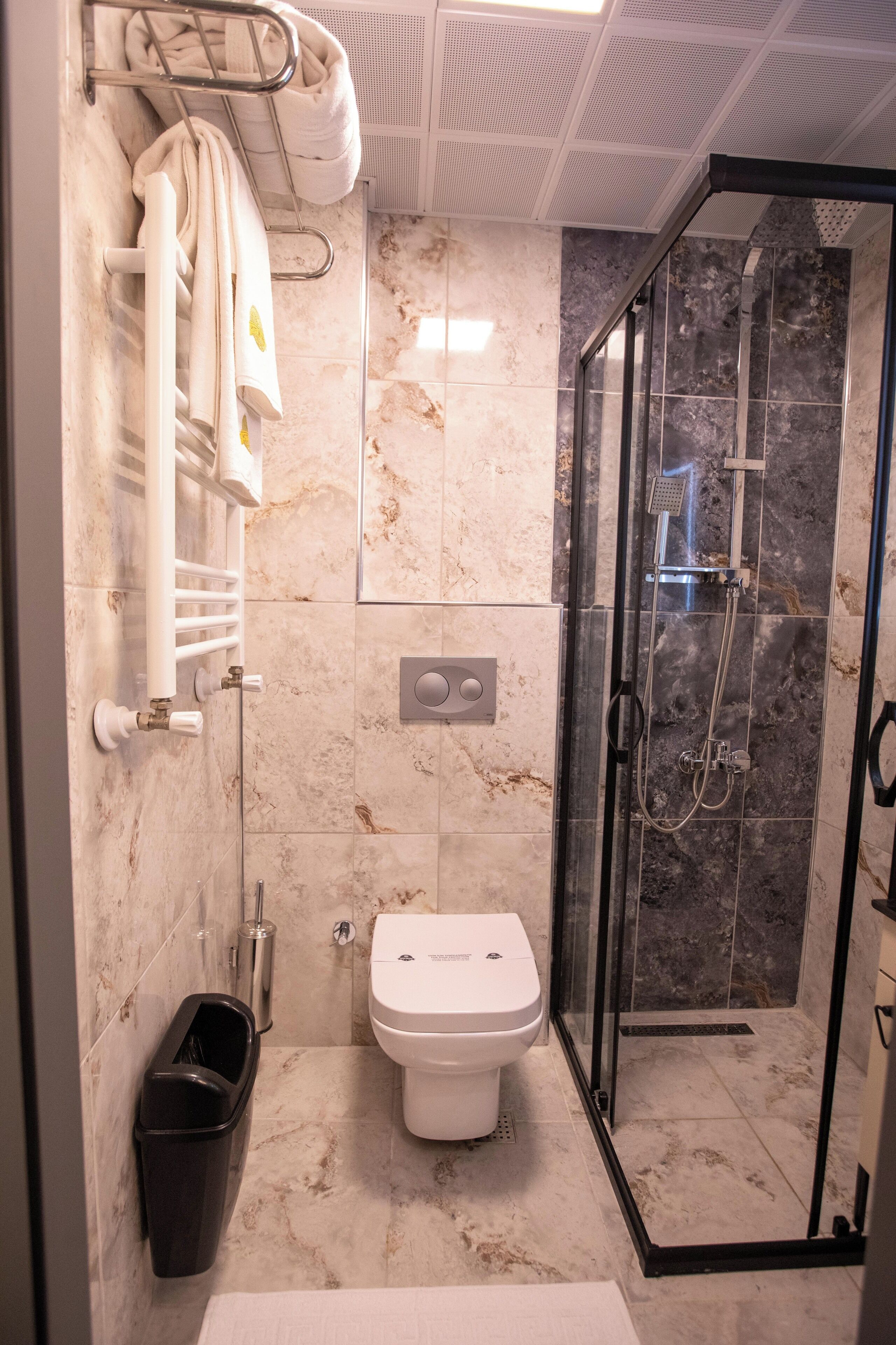 A modern bathroom with a glass-enclosed shower, a toilet, and a towel rack with multiple towels.