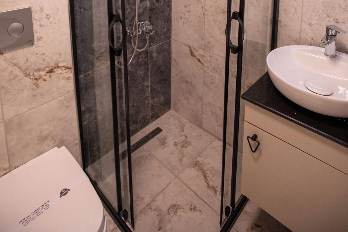 A modern bathroom with a glass-enclosed shower, a white sink, and a marble-tiled wall.