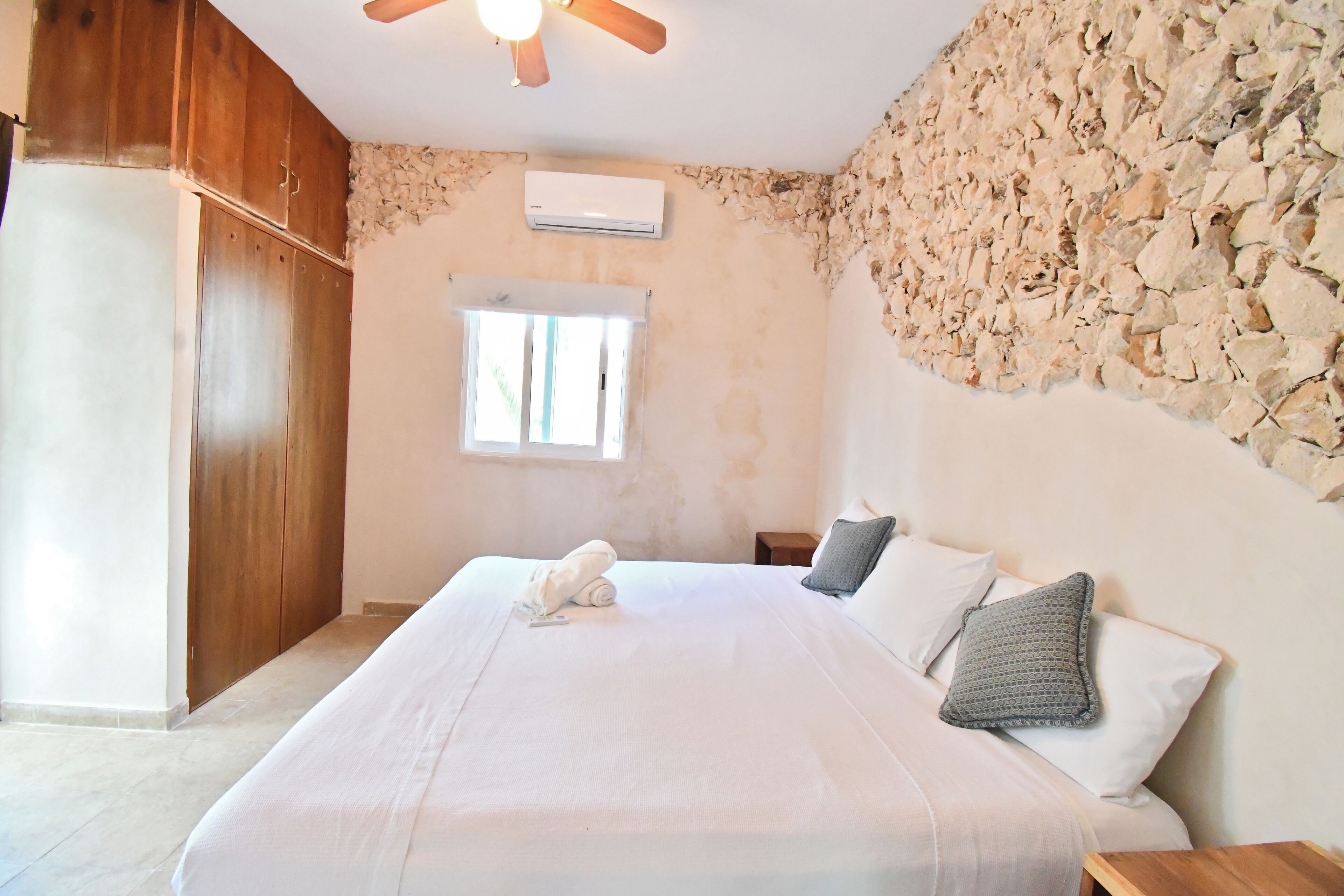 Un dormitorio con cama, armario de madera, pared de piedra y equipo de aire acondicionado.