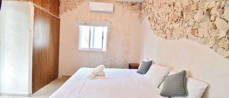 Un dormitorio con cama, armario de madera, pared de piedra y equipo de aire acondicionado.