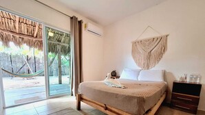 Un dormitorio con cama, mesita de noche, un tapiz de macramé y vistas a una hamaca en el exterior.