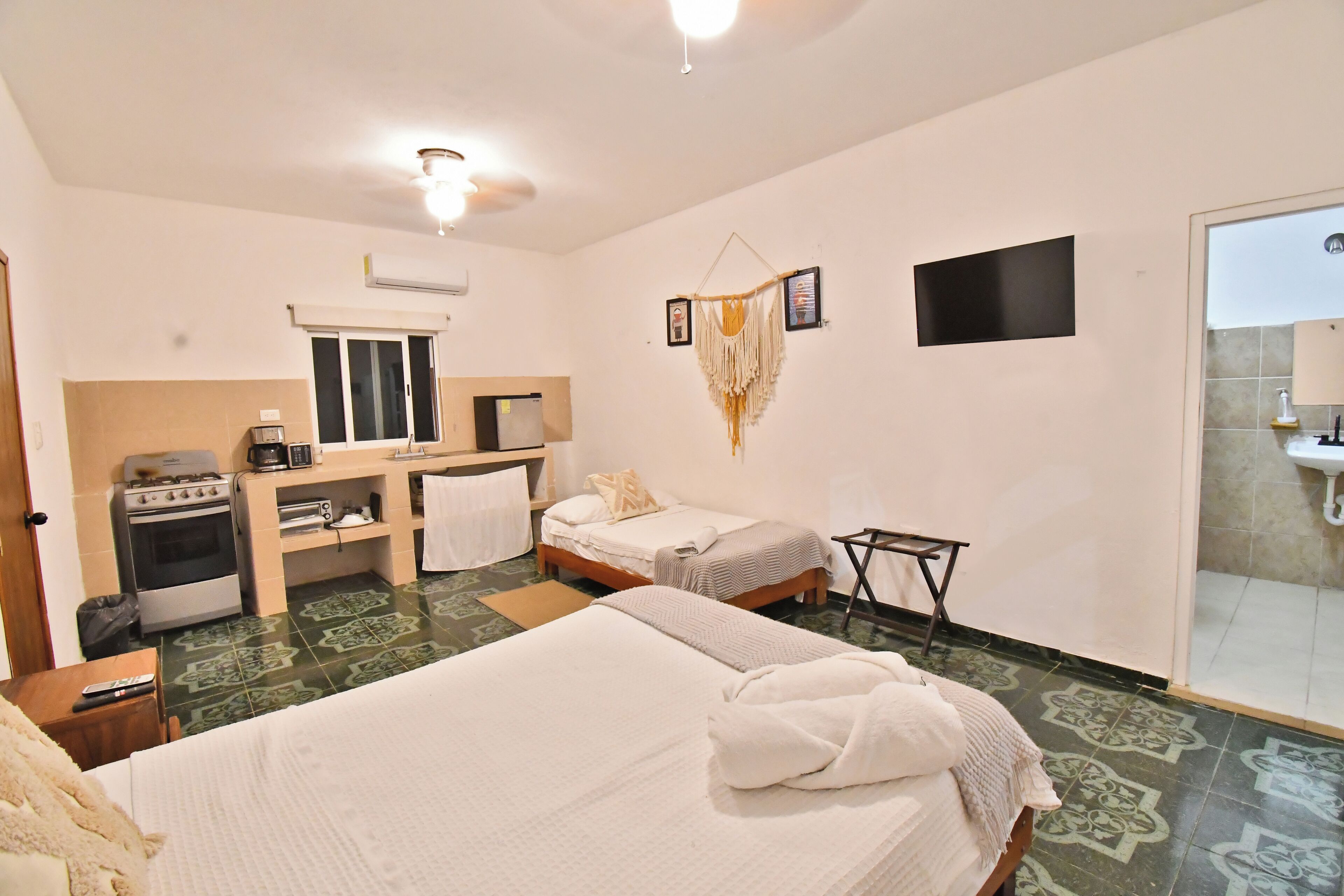 A hotel room with two beds, a kitchenette, a TV, and a bathroom with a sink and mirror.