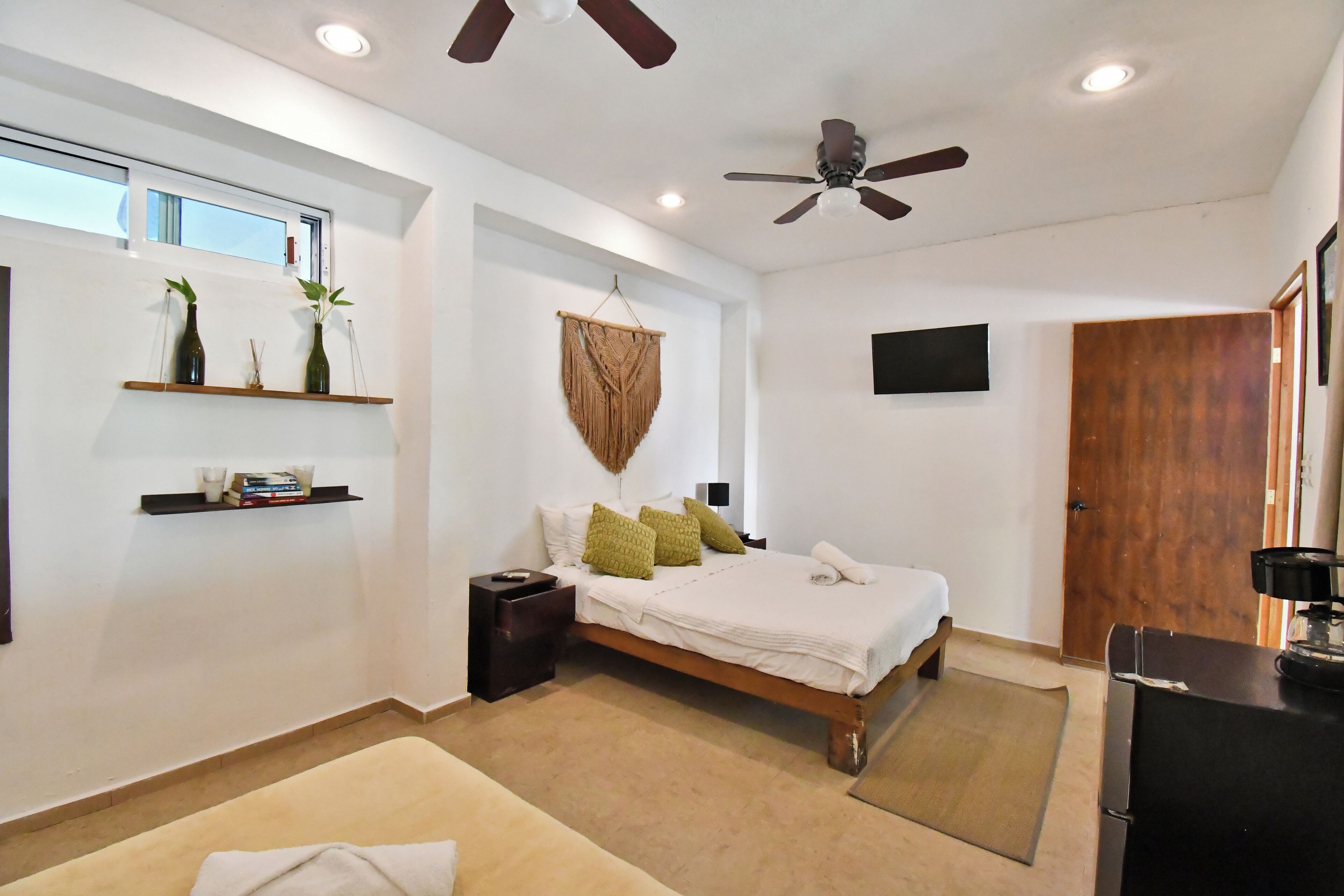Une chambre moderne comprenant un lit, des tables de chevet, un ventilateur de plafond, un téléviseur fixé au mur et une fenêtre avec des stores.