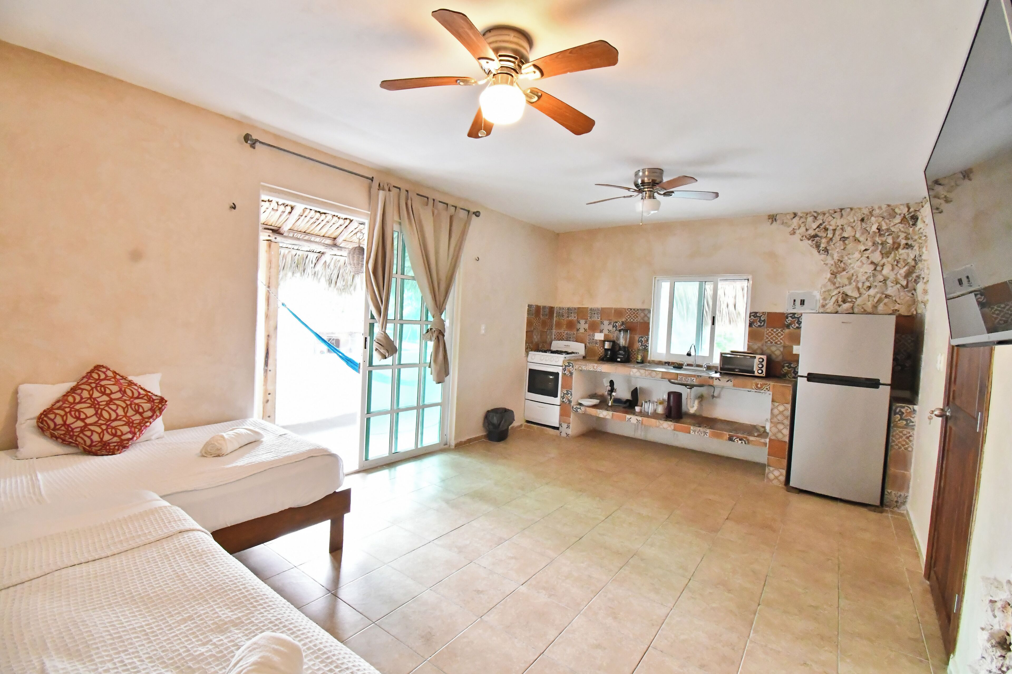 A hotel room with a bed, a ceiling fan, a kitchenette, and a bathroom with a shower.