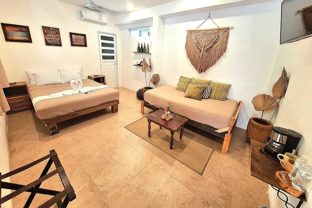 Una habitación acogedora con una cama, un sofá, una mesita de centro y un televisor. Hay cuadros enmarcados en la pared y una ventana con cortinas.