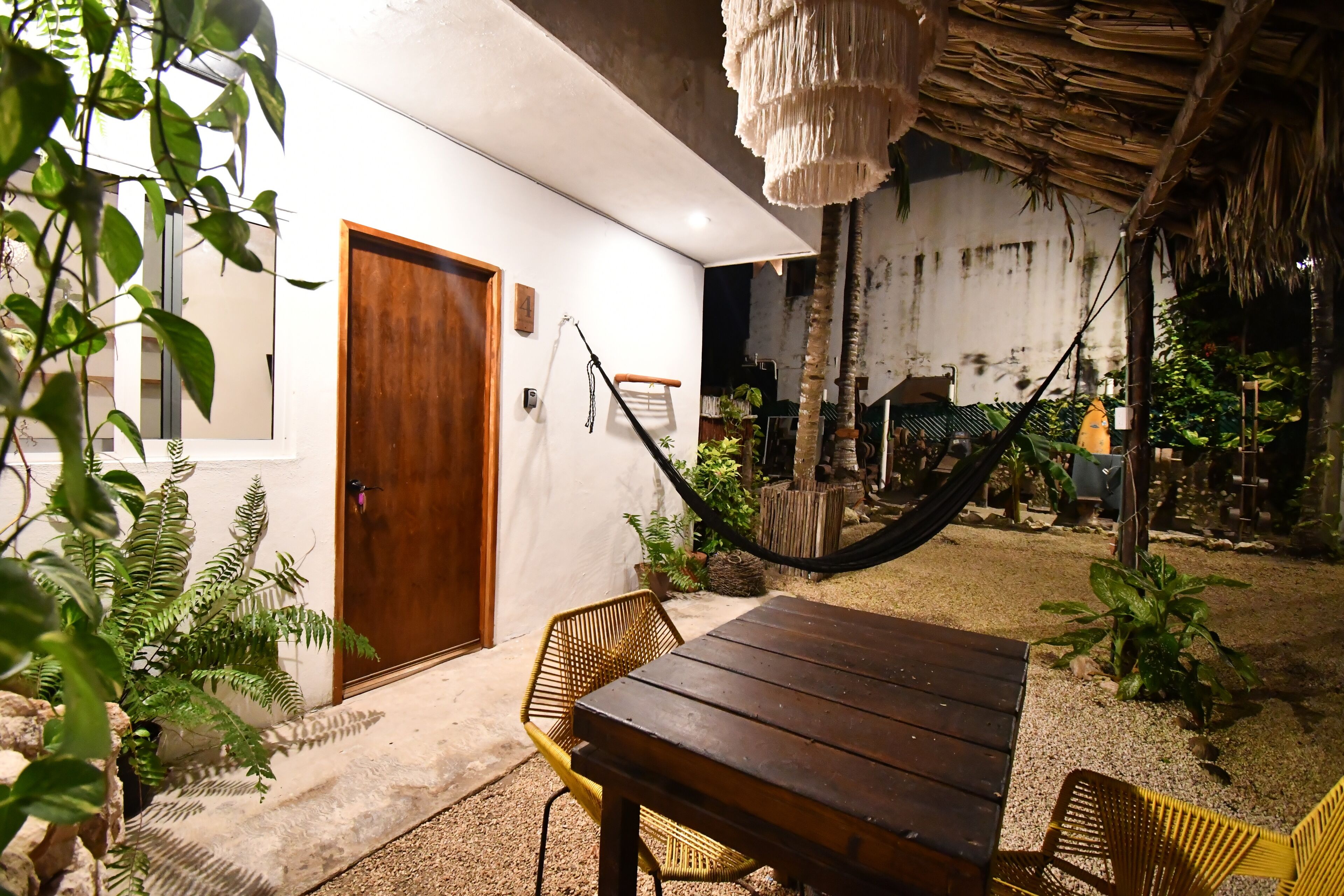 Une table et des chaises en bois se trouvent devant un bâtiment. On aperçoit une porte et un numéro sur le mur.
