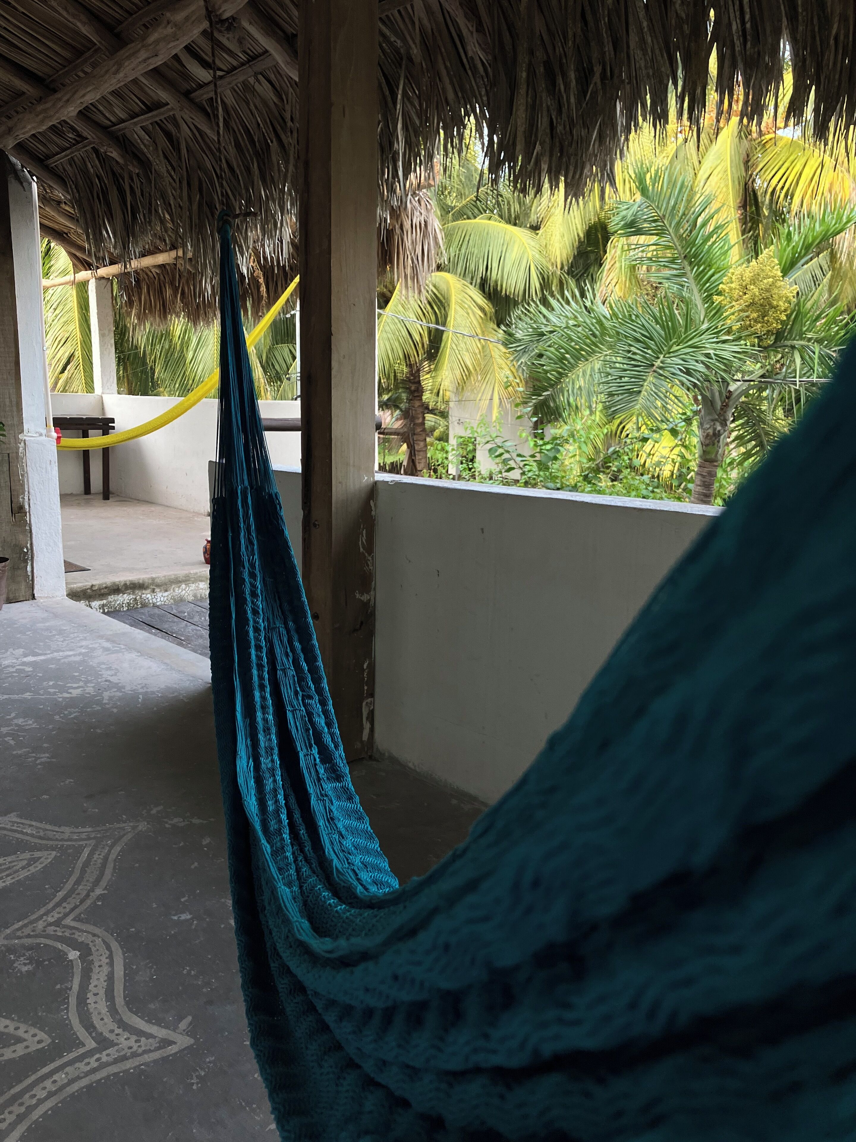 A hammock under a thatched roof, a bench, and a view of palm trees.