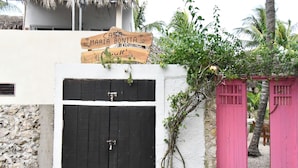 Una verja negra con un cartel de madera encima, una verja rosa y un muro de piedra.