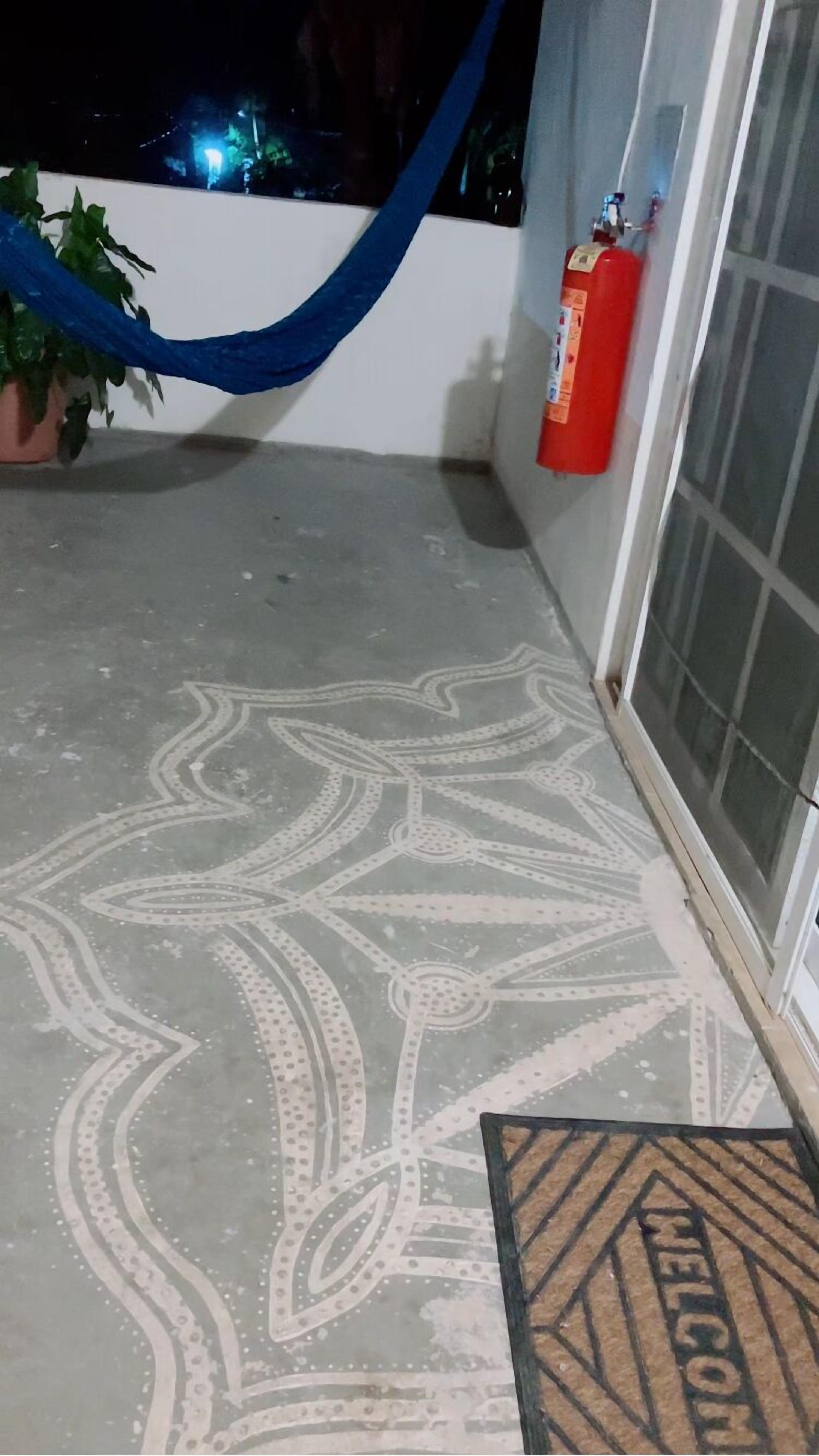 Un balcon avec un sol à motifs, un tissu bleu, une plante en pot, un extincteur et un paillasson.