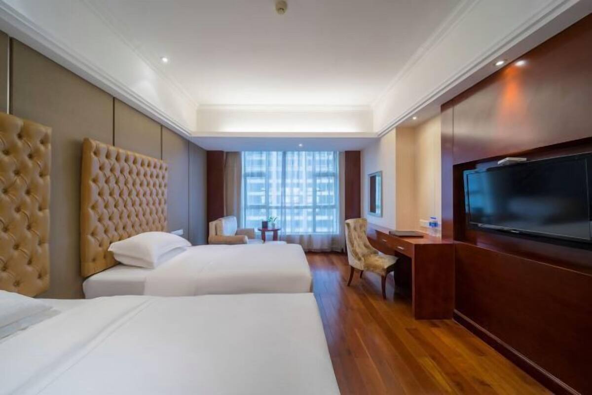 A hotel room with two beds, a desk, a chair, a television, and a large window.