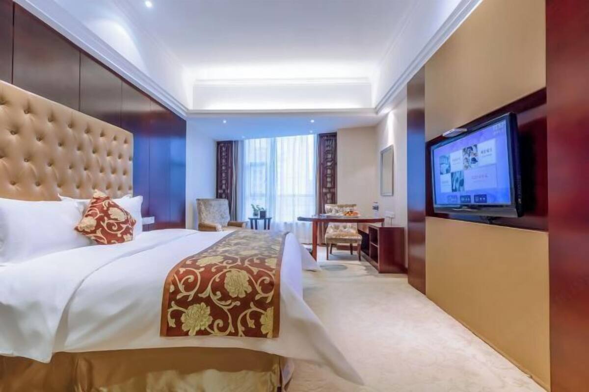 A hotel room with a large bed, a television, a desk, and a chair.