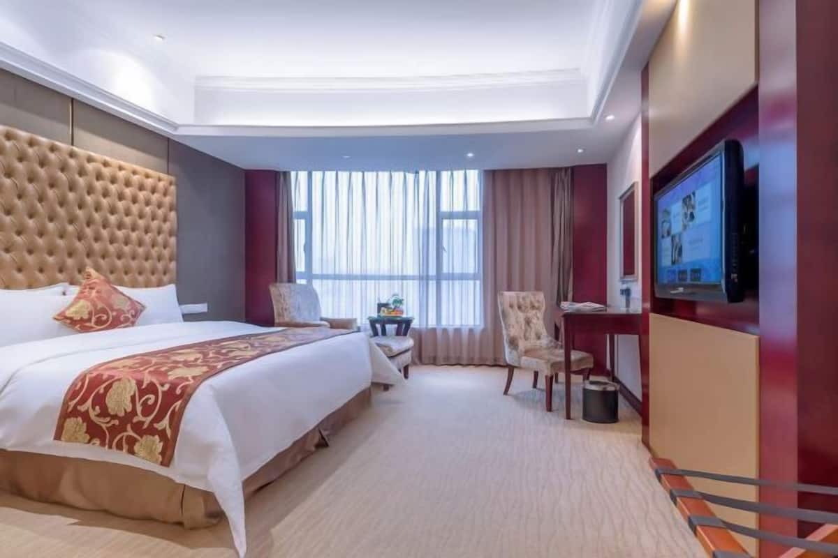 A hotel room with a large bed, a TV, a desk, and a chair.