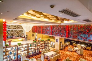 Un hall d'hôtel au design moderne, avec un mur décoré de motifs, un comptoir d'accueil et un espace détente comprenant des tables et des chaises.