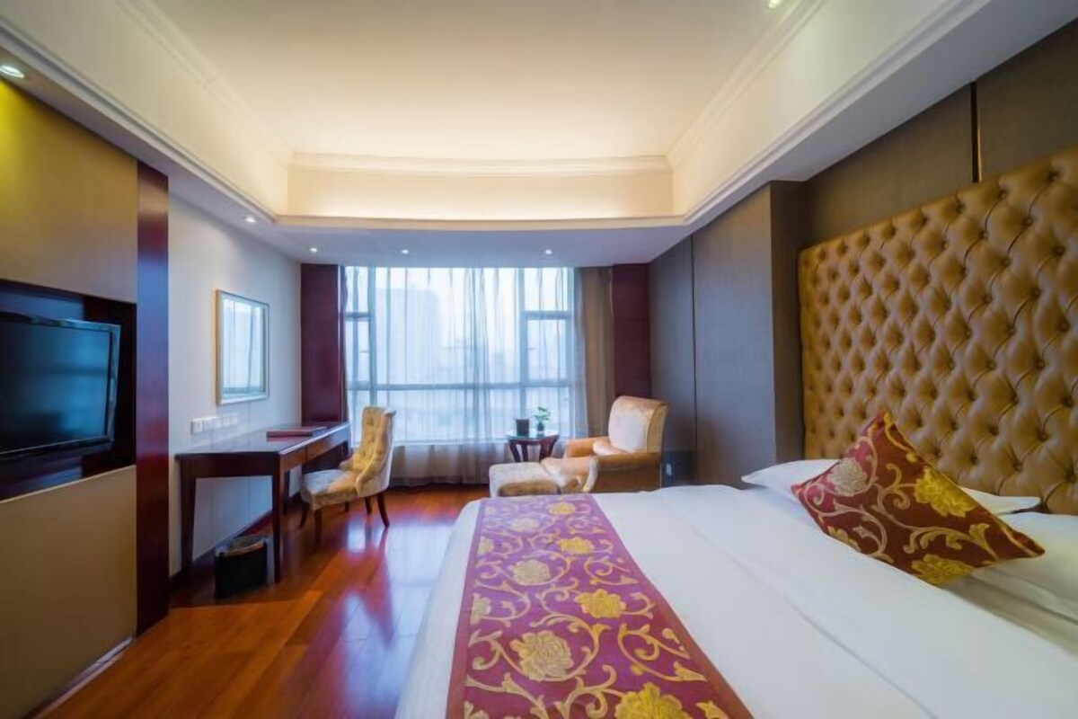 A hotel room with a large bed, a TV, a desk, and a chair.