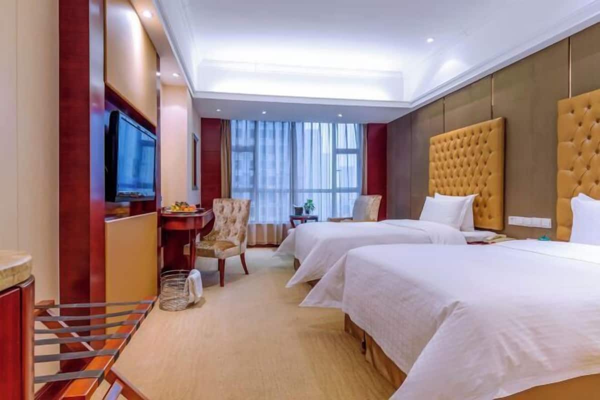 A hotel room with two beds, a TV, a desk with a chair, and a large window.