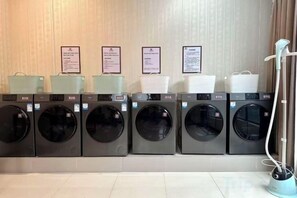 A row of front-loading washing machines with hanging baskets above them.