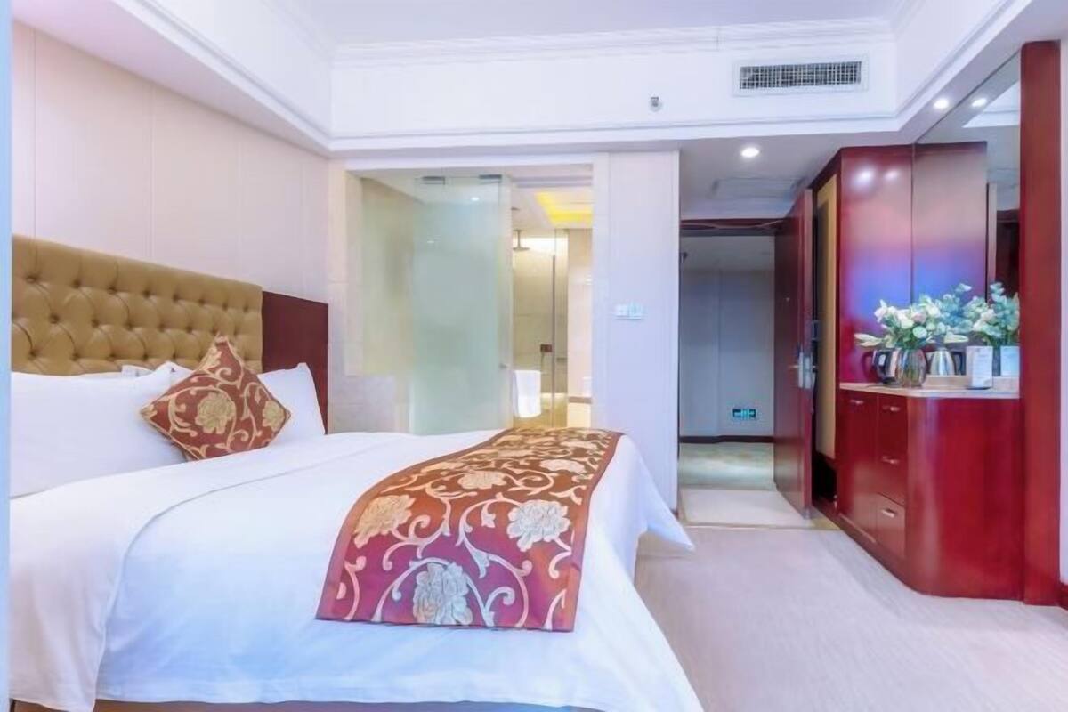 A hotel room with a large bed, a red and gold decorative throw, a wooden headboard, and a red wardrobe with a mirror.