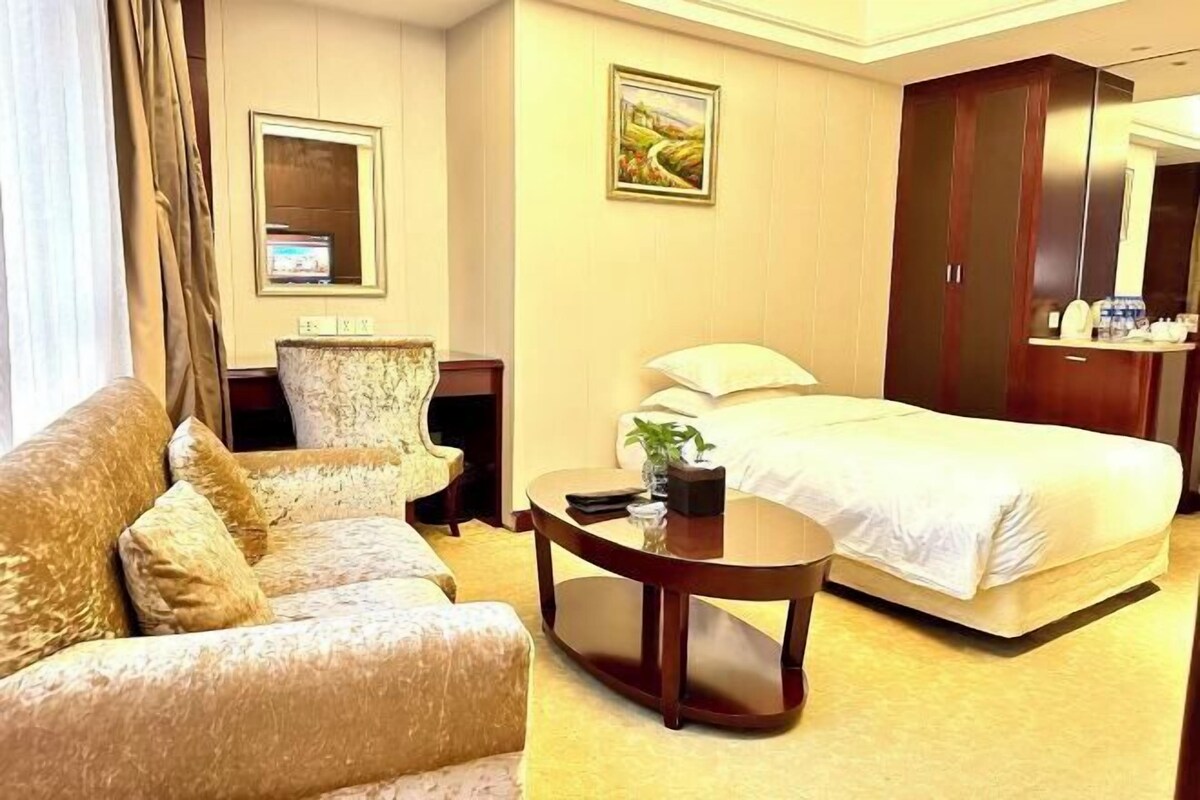 A hotel room with a bed, a sofa, a coffee table, a TV, and a painting on the wall.
