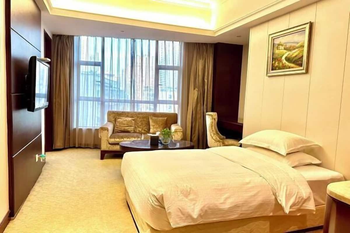 A hotel room with a large bed, a sofa, a small table, and a TV.