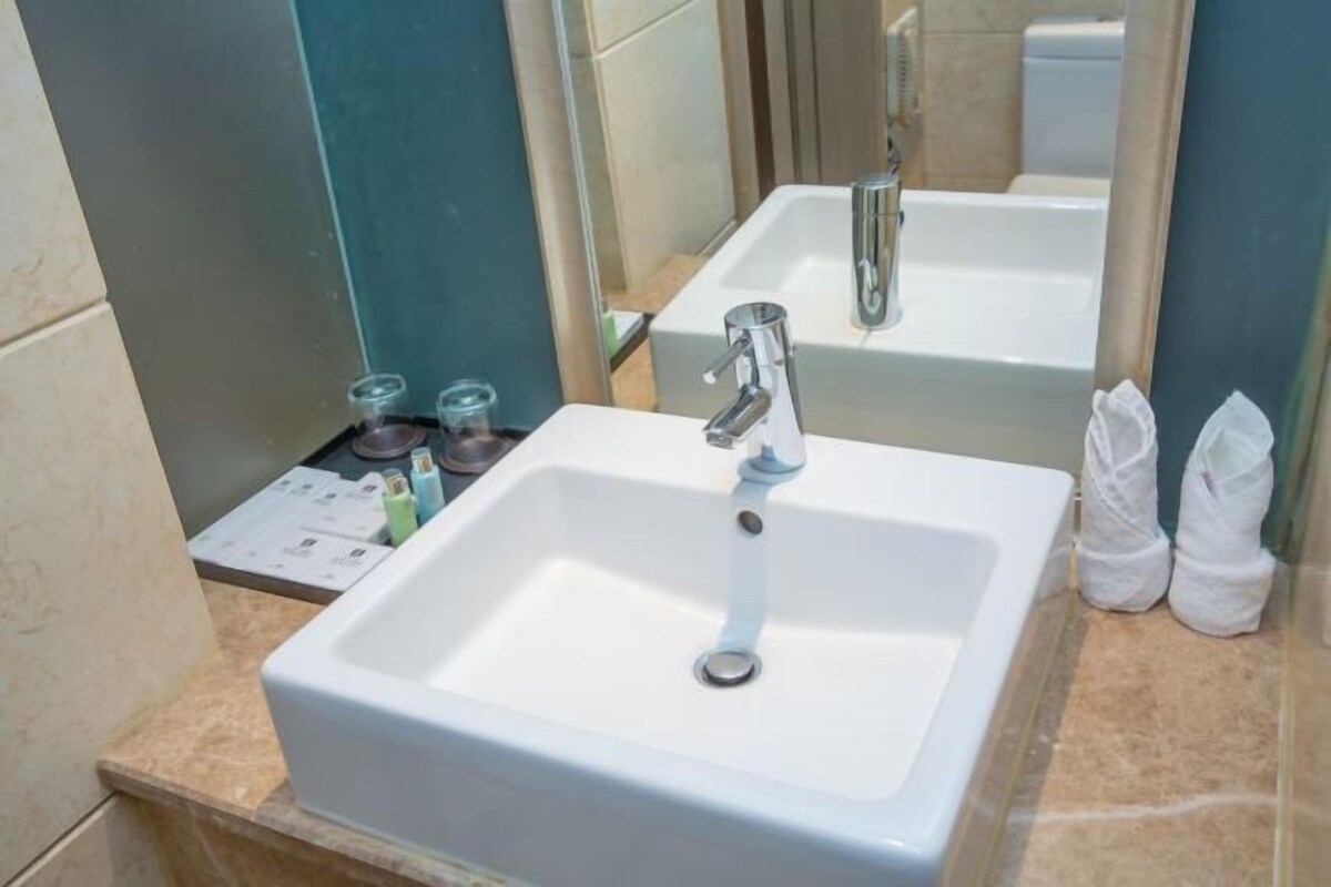 A bathroom with a white sink, a mirror, and a bathtub. There are toiletries on the counter.