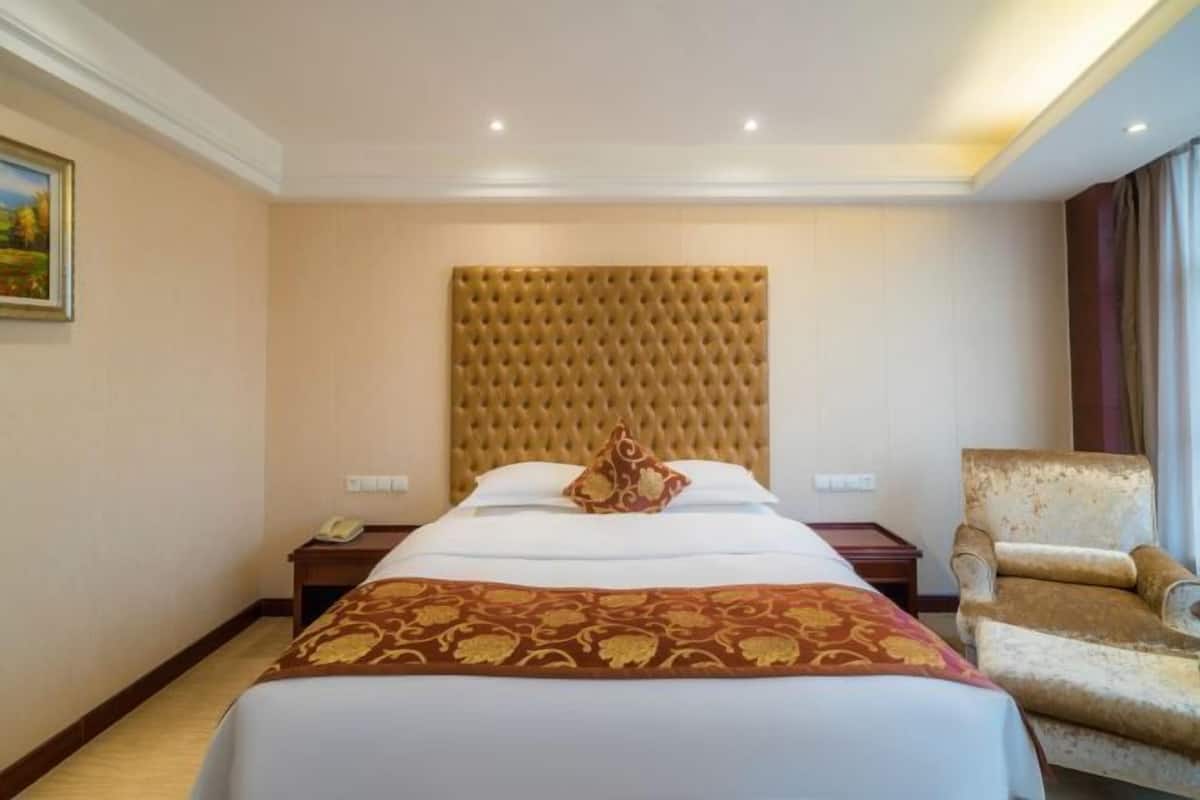 A hotel room with a large bed, a headboard, a bedside table with a phone, and a chair.