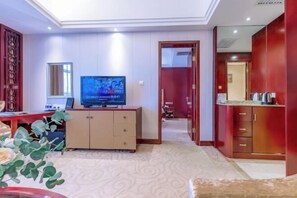 A hotel room with a TV, a desk, a cabinet, and a red wardrobe.
