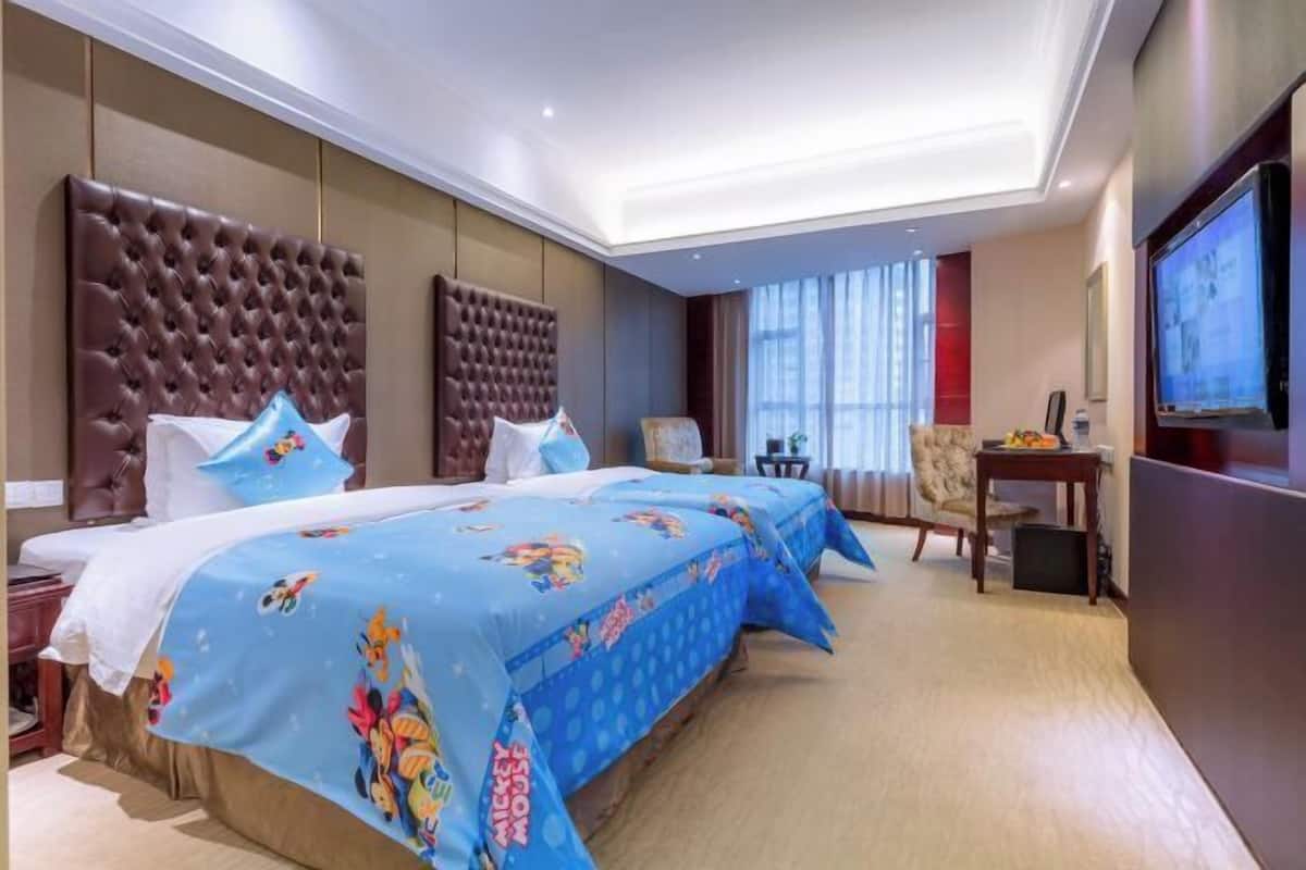 A hotel room with two beds, a television, a desk, and a window with curtains.