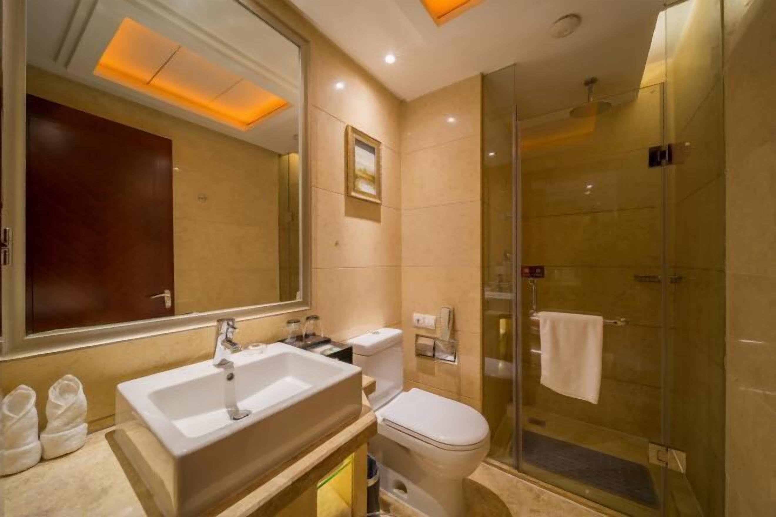 A modern bathroom with a large mirror, a sink, a toilet, and a glass-enclosed shower.