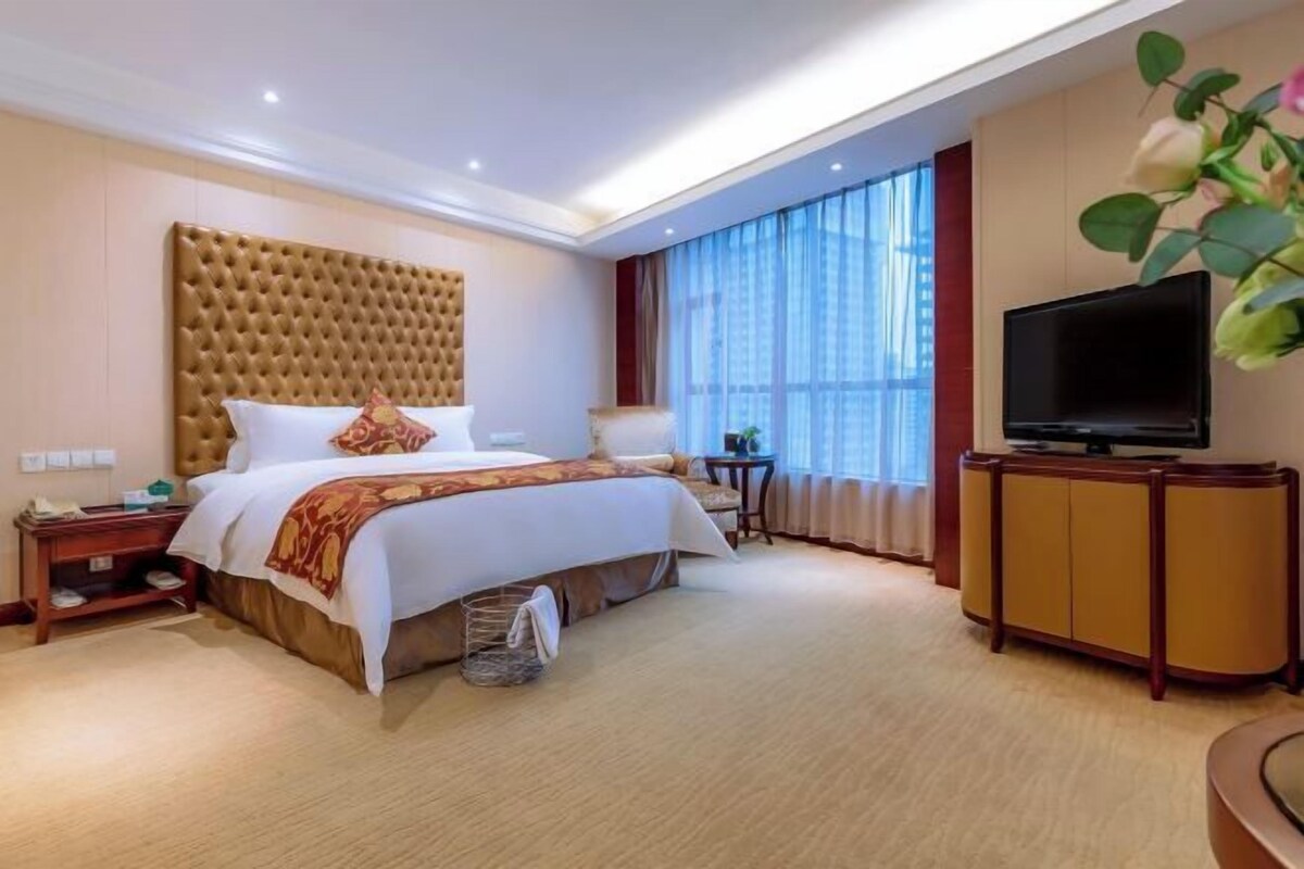 A hotel room with a large bed, a television, a small table, and a cabinet.